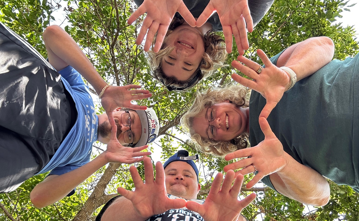 Circle of people smiling and holding out hands, photo taken from below